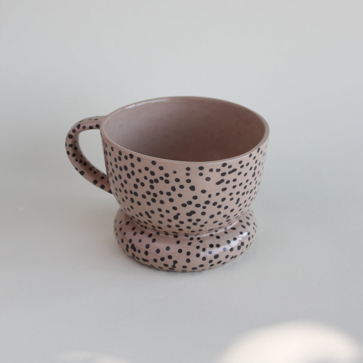 Ceramiczny kubek OJ Kropki, widok z przodu z widocznym wnętrzem, różowawa kamionka z czarnymi kropkami, ręcznie robiony Tokiart