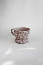 Ceramiczny kubek OJ Kropki, widok z boku pod kątem, różowawa kamionka z czarnymi kropkami w masie, ręcznie robiony w pracowni Tokiart