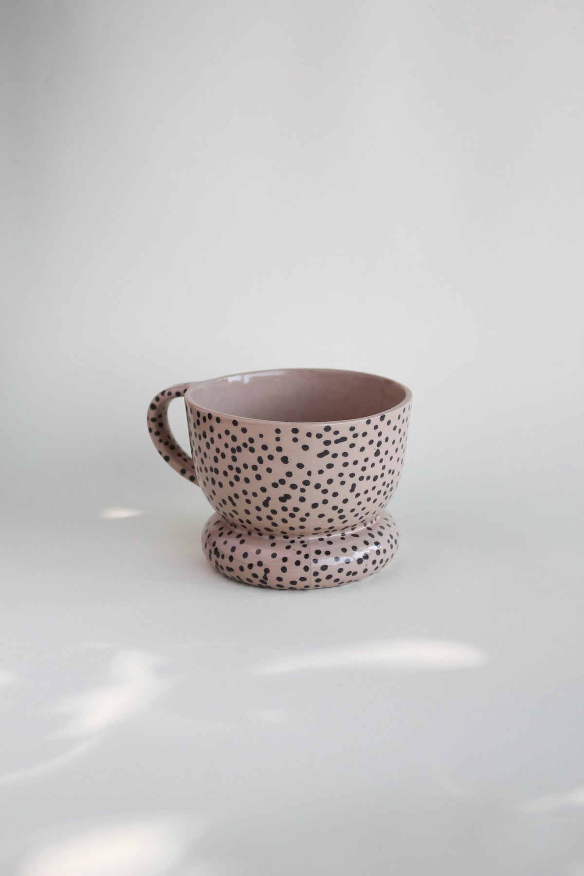 Ceramiczny kubek OJ Kropki, widok z boku pod kątem, różowawa kamionka z czarnymi kropkami w masie, ręcznie robiony w pracowni Tokiart